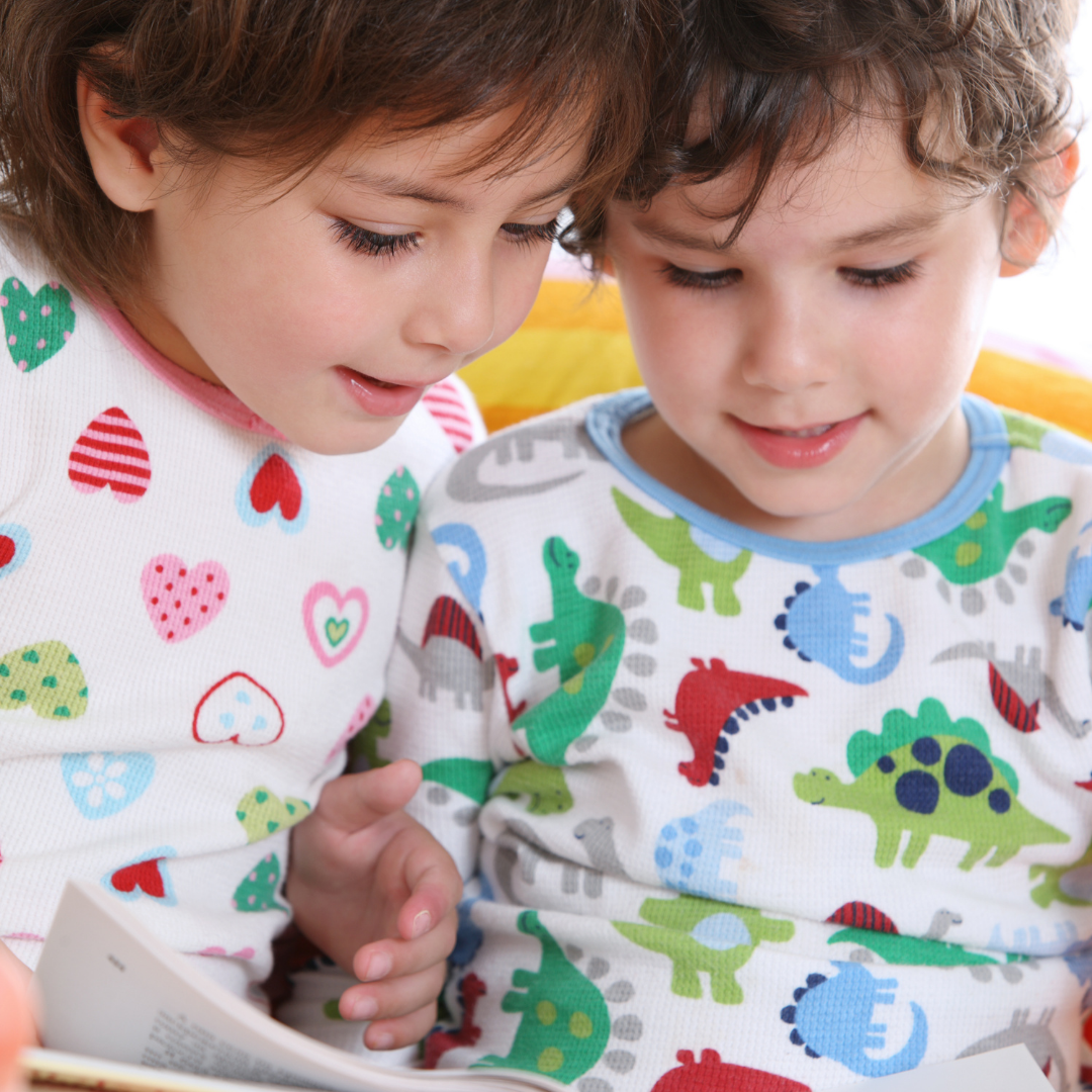 2 children in pajamas looking at a book