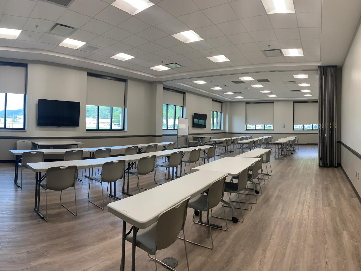 Long room with two televisions mounted on the walls, tables setup in rows.