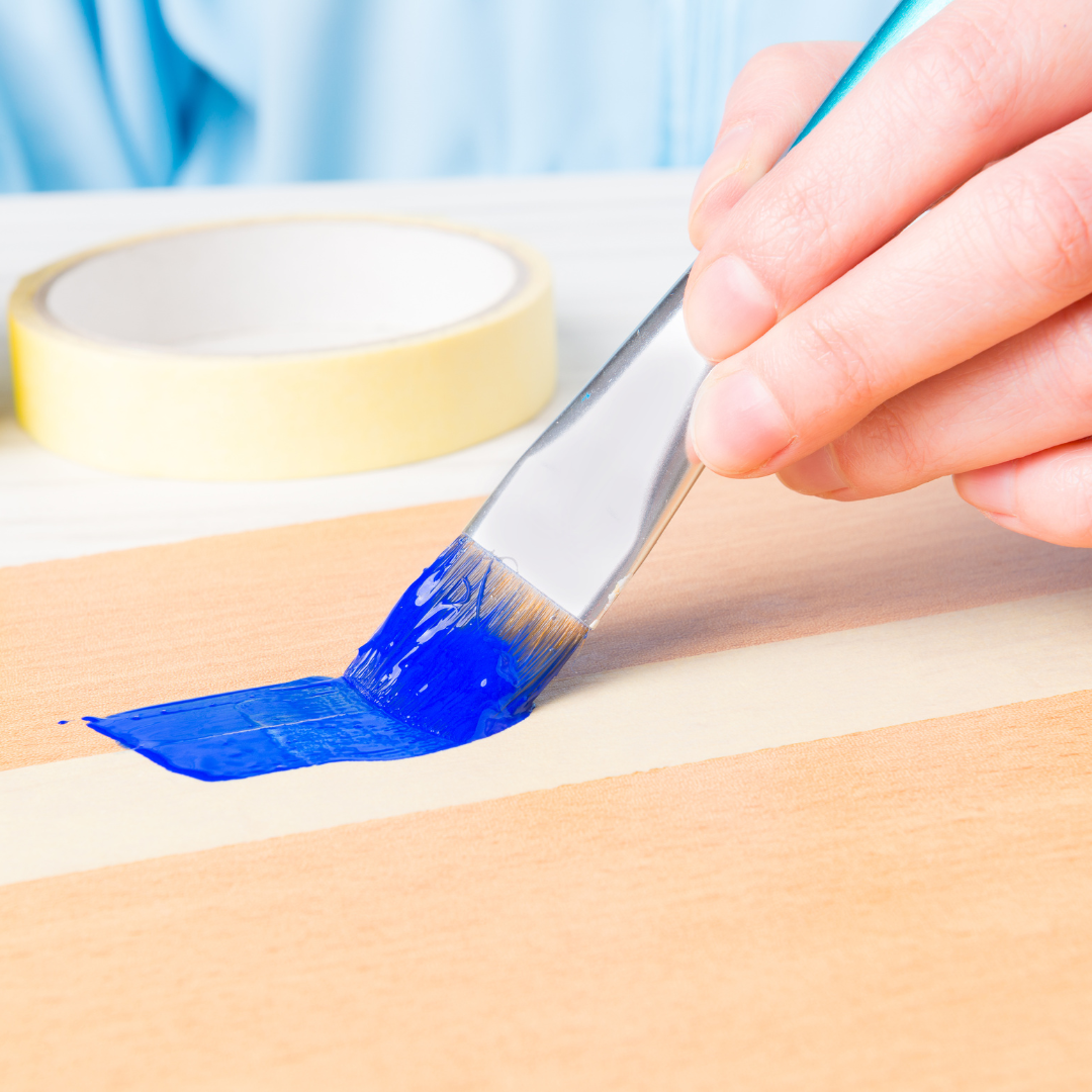 Hand drawing a paint-covered brush along a strip of masking tape.